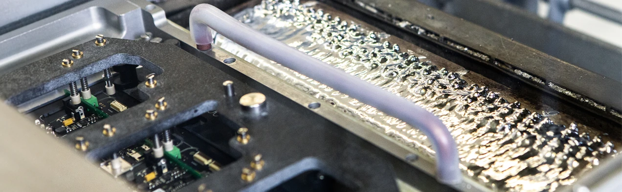 Cette image montre un cadre de soudure plongeant dans une vague de soudure liquide dans une machine de soudure à la vague, typique pour les processus de fabrication THT chez Cloos Electronic. Elle illustre l'application précise de la technologie de soudure pour la production de cartes électroniques de haute qualité.