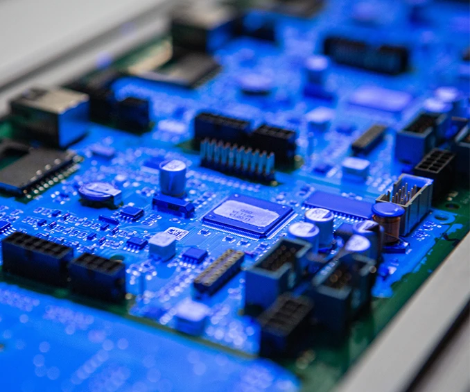 Inspection UV de cartes électroniques revêtues de vernis protecteur, équipées de SMD et THT pour le contrôle de qualité. Après l'assemblage SMD, les cartes sont vernies dans la machine de revêtement sélectif et contrôlées sur le tapis de sortie.