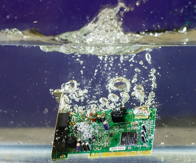 Photo d'une carte électronique SMD de CLOOS electronic, entourée d'eau, pour démontrer l'effet protecteur du revêtement de parylène. Cette image illustre de manière impressionnante comment le revêtement protège les composants électroniques de l'humidité, assurant fiabilité et longévité dans des environnements exigeants.